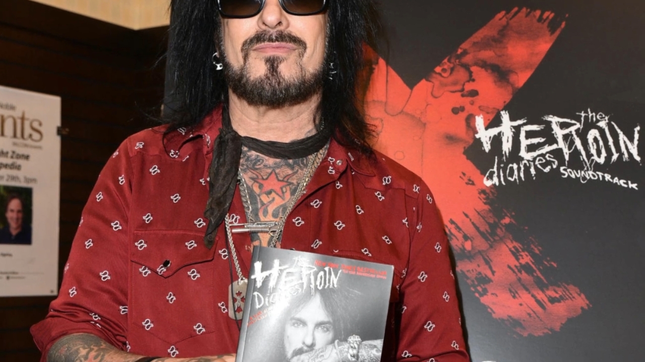 Nikki Sixx in sunglasses holds a book at a promotional event