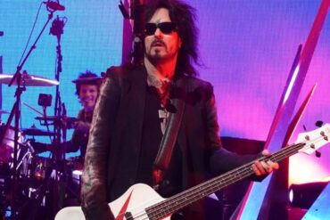 Nikki Sixx in sunglasses plays a white bass guitar onstage