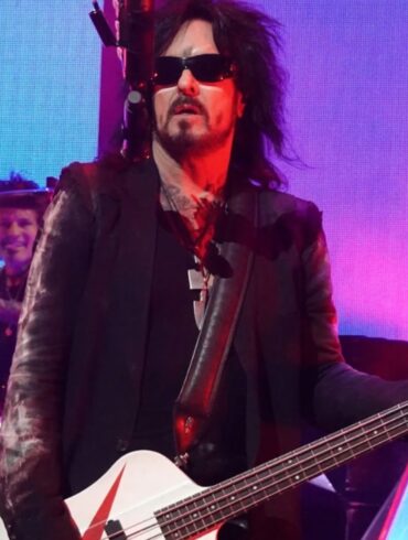 Nikki Sixx in sunglasses plays a white bass guitar onstage