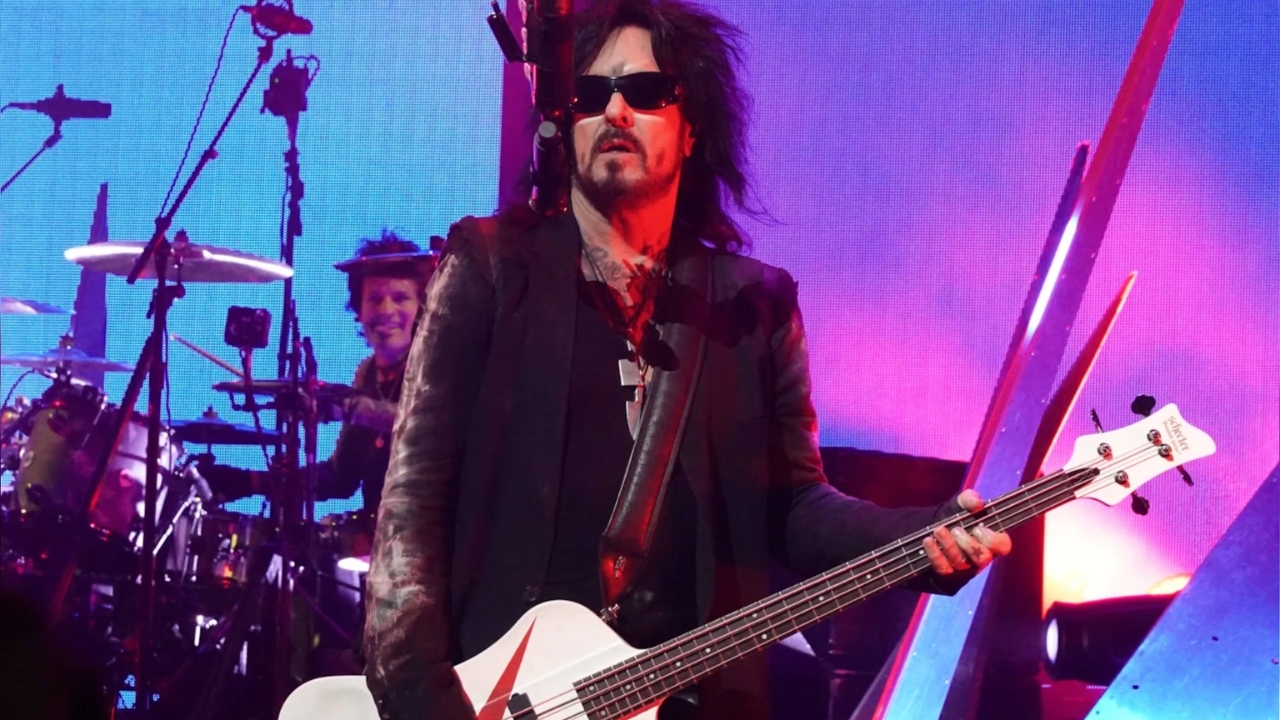 Nikki Sixx in sunglasses plays a white bass guitar onstage
