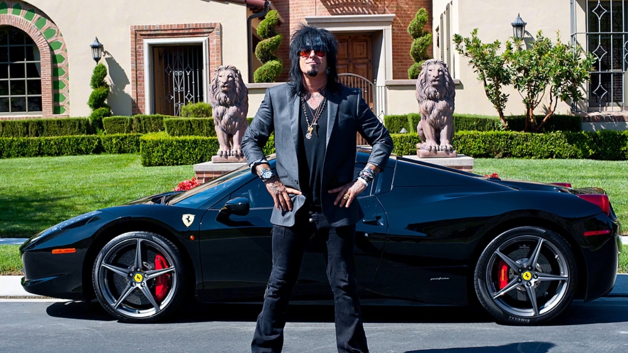 Nikki Sixx poses beside a black Ferrari outside a luxury home