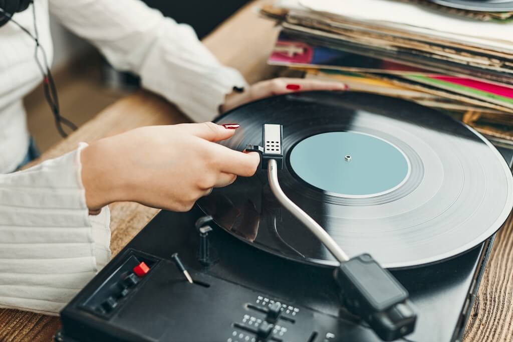 Person placing needle on vinyl record on a turntable, close-up of analog music playback