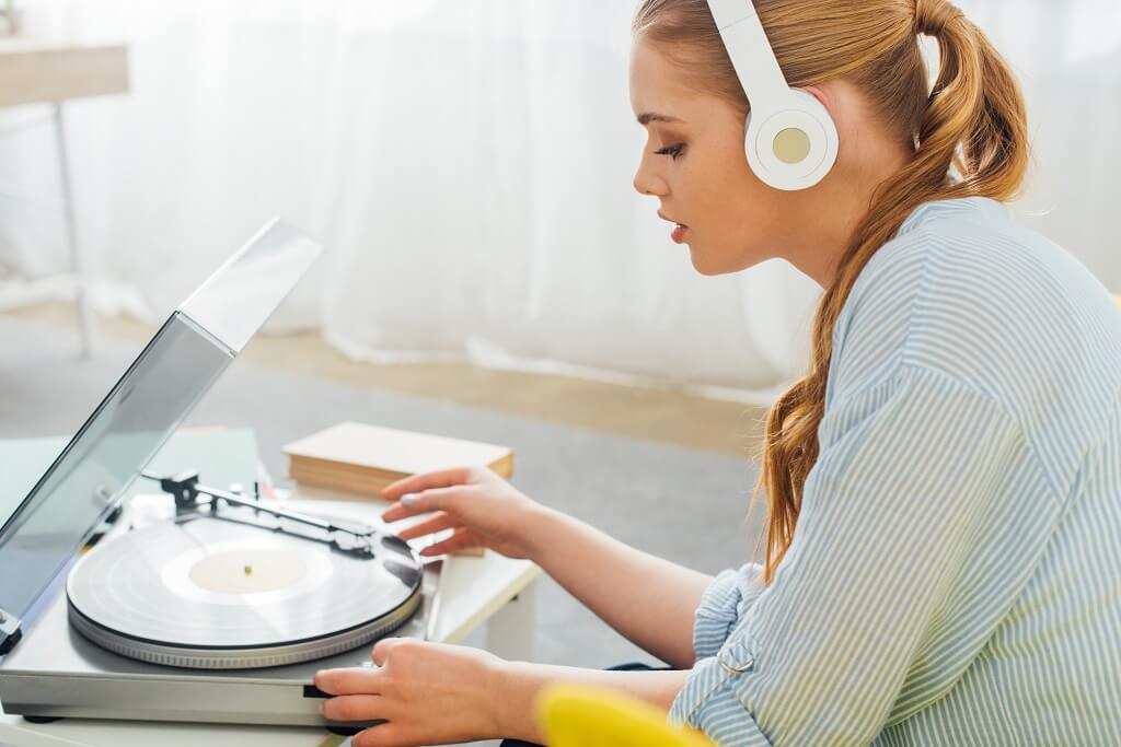 Woman listening to vinyl record on turntable while wearing headphones at home
