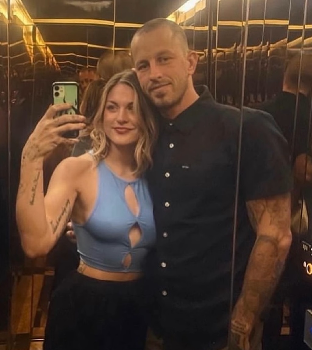 Frances Bean Cobain taking a mirror selfie in an elevator with husband Riley Hawk, both smiling and dressed casually