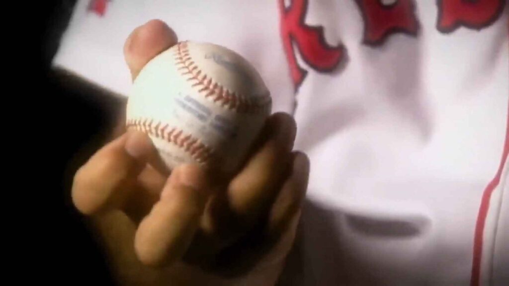 Close-up of a hand holding a baseball with a knuckleball grip in a Red Sox jersey