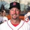 Baseball player in a Red Sox uniform smiling, with family and a championship trophy in the background
