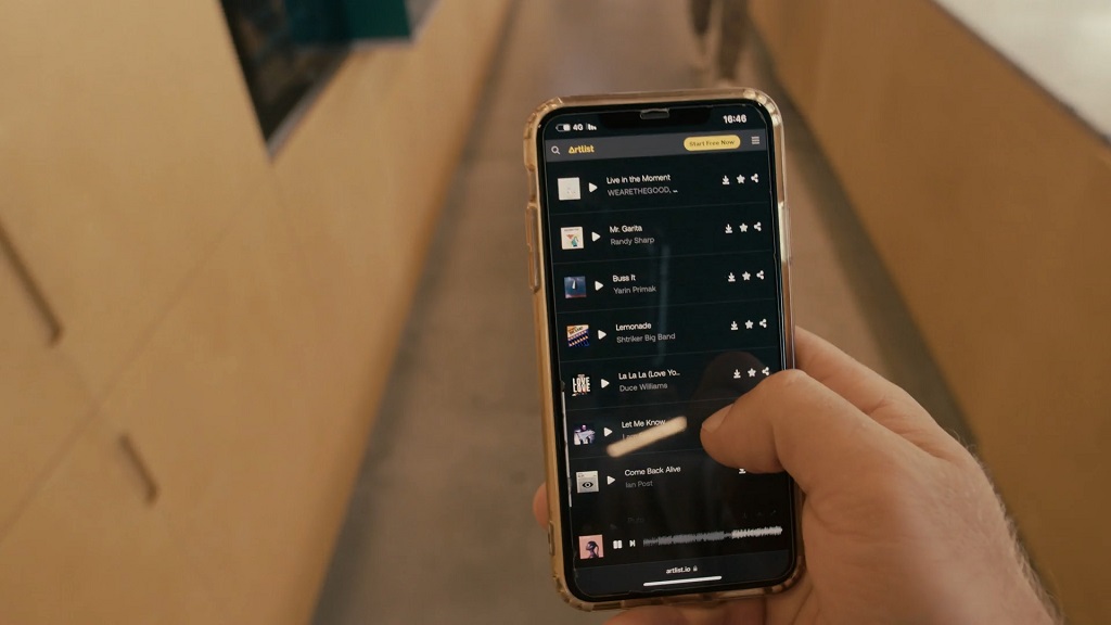 Close-up of a person holding a smartphone displaying a music app with a playlist of songs