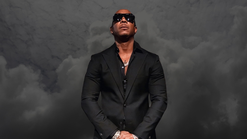 Ja Rule stands in a black suit and sunglasses against a cloudy backdrop