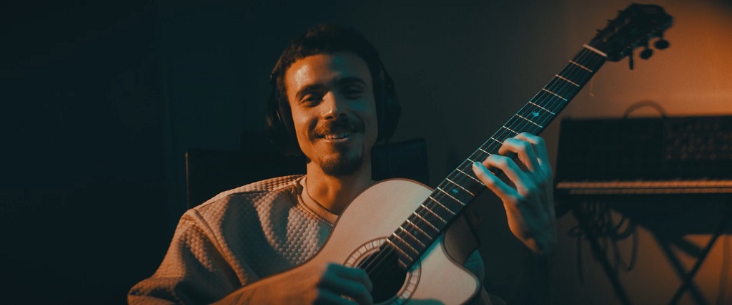 Smiling musician wearing headphones while playing an acoustic guitar in a dimly lit studio