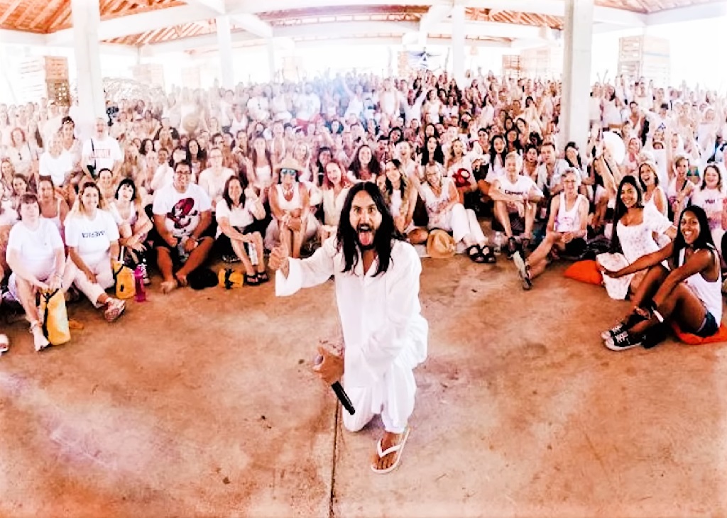 Jared Leto in white clothing kneeling with a microphone, surrounded by a large crowd of fans also dressed mostly in white