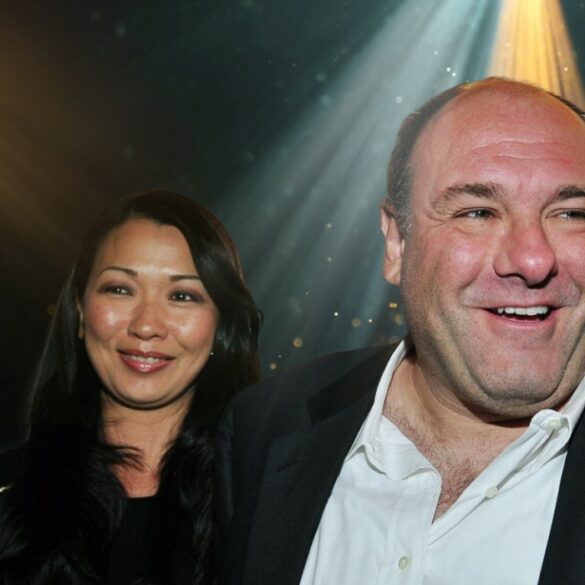 Actor James Gandolfini smiling in a suit with his wife Deborah Lin standing beside him at an event, illuminated by stage lights