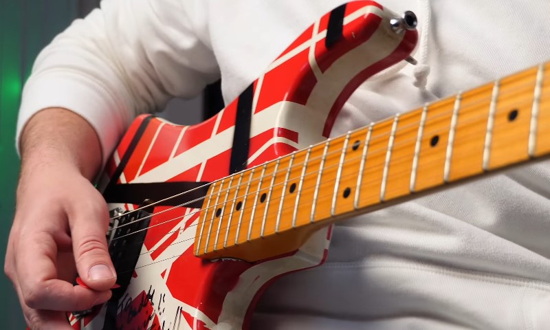 How Eddie Van Halen Built the Frankenstrat and Changed Rock Forever Close-up of a hand striking strings on a red, white, and black striped electric guitar