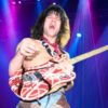 van Halen shirtless on stage under vibrant blue and magenta spotlights, holding a striped red and white electric guitar