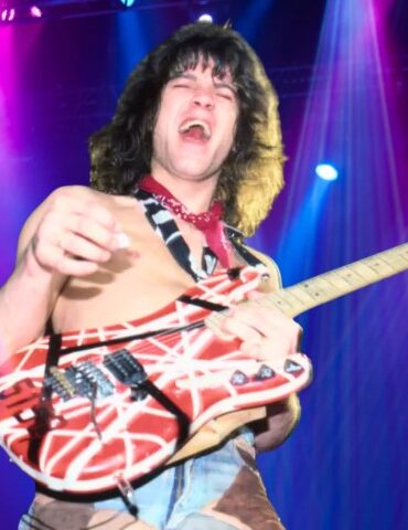 van Halen shirtless on stage under vibrant blue and magenta spotlights, holding a striped red and white electric guitar