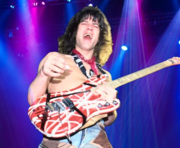van Halen shirtless on stage under vibrant blue and magenta spotlights, holding a striped red and white electric guitar