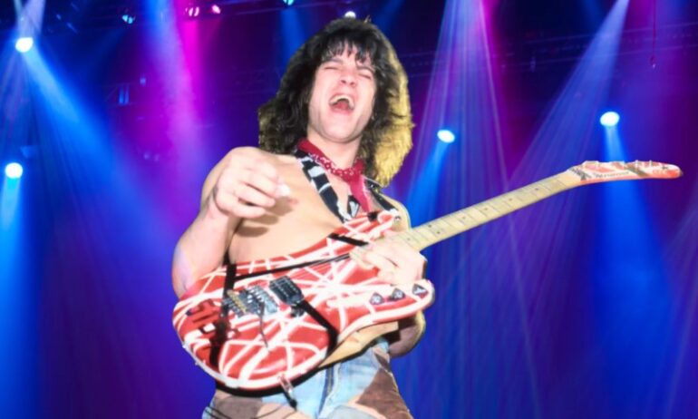 How Eddie Van Halen Built the Frankenstrat and Changed Rock Forever van Halen shirtless on stage under vibrant blue and magenta spotlights, holding a striped red and white electric guitar