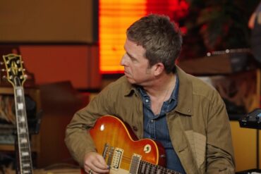 Noel Gallagher Biography - The Songwriter Who Defined Britpop Noel Gallagher sits in a studio holding his guitar during a recording session