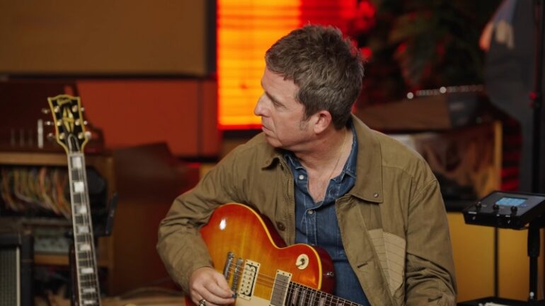 Noel Gallagher Biography - The Songwriter Who Defined Britpop Noel Gallagher sits in a studio holding his guitar during a recording session