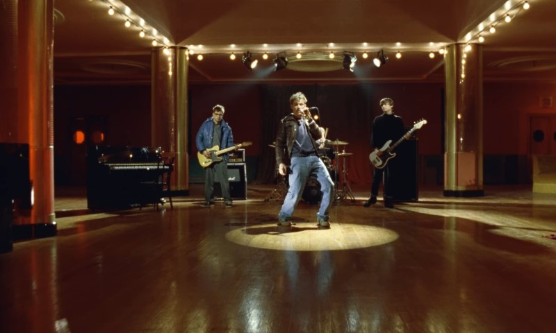 "Blur" rock band performing energetically in a dimly lit, empty ballroom