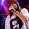 Axl Rose singing on the stage during a concert, wearing white shirt and red bandana