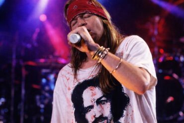 Axl Rose singing on the stage during a concert, wearing white shirt and red bandana