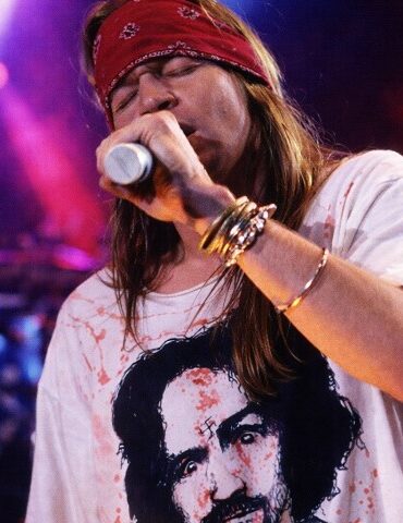 Axl Rose singing on the stage during a concert, wearing white shirt and red bandana