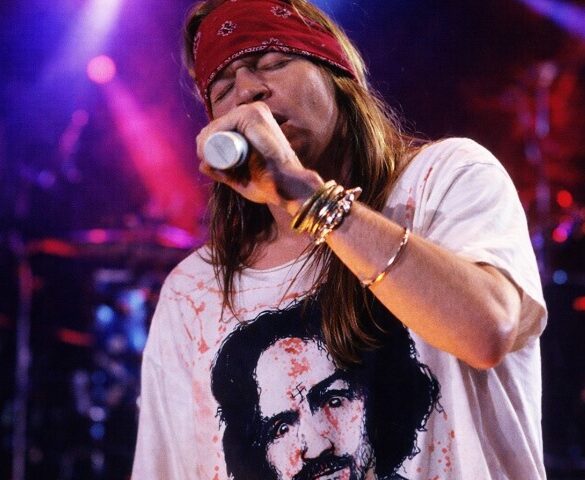 Axl Rose singing on the stage during a concert, wearing white shirt and red bandana