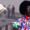Afroman holding a decorated cup with police scene and money imagery in the background
