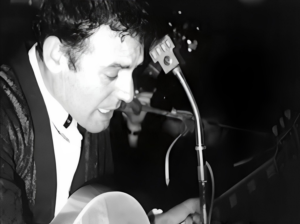 Black and white photo of rockabilly musician Carl Perkins singing and playing guitar at a microphone