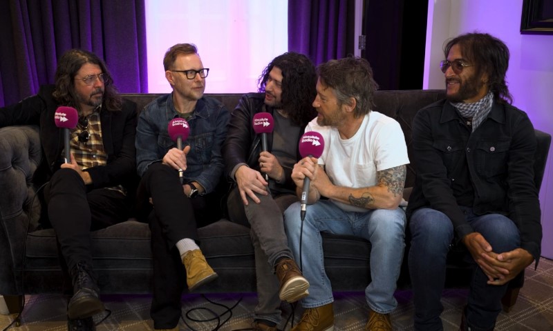 Foo Fighters Your Favorite Toy - Release Date, Tracklist, and What To Expect Foo Fighters lineup sit on a couch holding purple microphones, engaged in a cheerful conversation