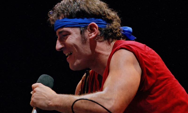 The Bandana in Rock Culture: 10 Iconic Moments That Defined a Generation Bruce Springsteen in a red tank top and blue bandana sings passionately into a microphone on stage
