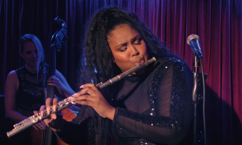 How Lizzo Helped Make Classical Training Feel Cool Again Lizzo passionately playing the flute on stage in a sparkling outfit