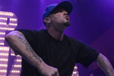 Fred Durst in a black shirt and blue cap performing energetically on stage