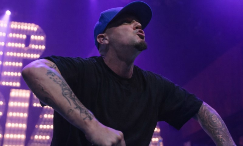 Fred Durst in a black shirt and blue cap performing energetically on stage