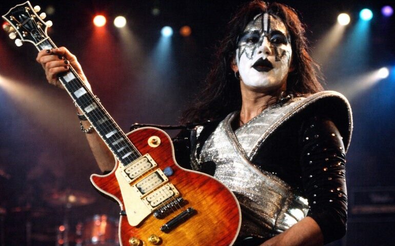 The Life and Career of Ace Frehley, the Guitarist Who Helped Shape the Sound of KISS A musician with dramatic black-and-white face paint and a shiny, silver costume plays an electric guitar on stage