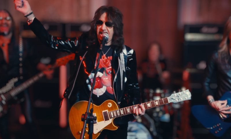 The Life and Career of Ace Frehley, the Guitarist Who Helped Shape the Sound of KISS A musician in sunglasses and a shiny black jacket plays a yellow electric guitar and sings into a microphone on stage