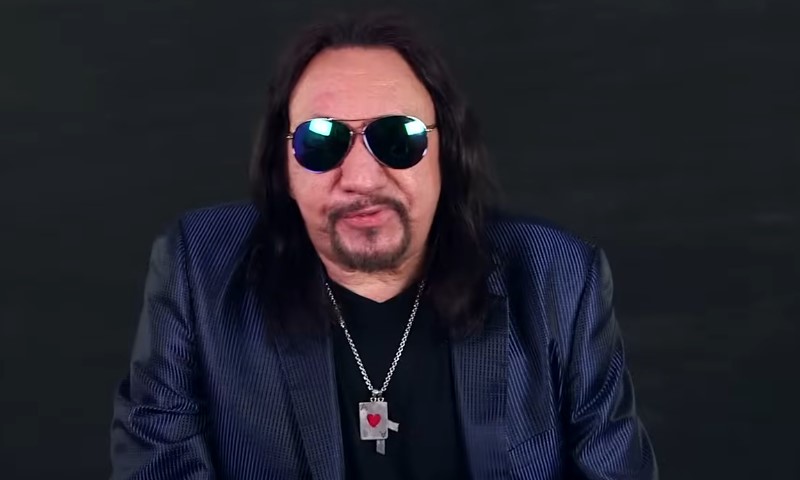 The Life and Career of Ace Frehley, the Guitarist Who Helped Shape the Sound of KISS Ace Frehley wearing sunglasses, a textured blue blazer, and a necklace with a heart pendant