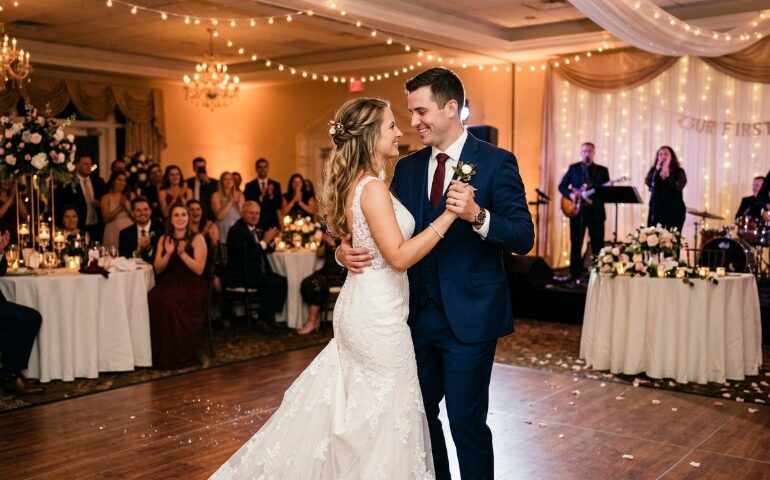 A bride in a lace gown and groom in a navy suit share a joyful first dance