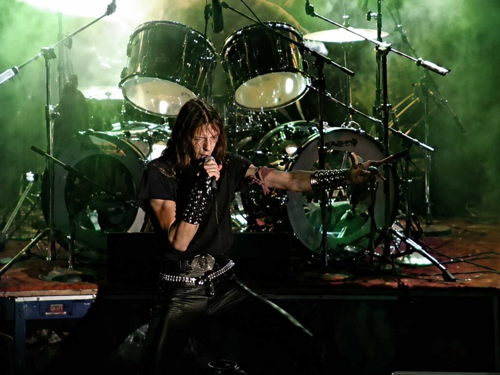 10 Rock and Metal Bands Inspired by Fantasy Books Metal singer performing in front of a large drum kit under green stage lights.