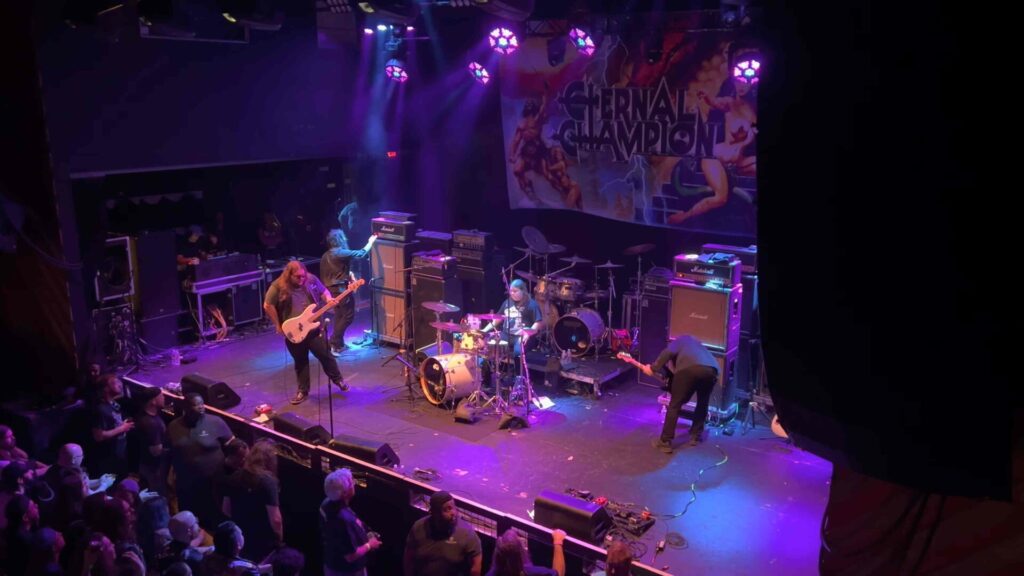 10 Rock and Metal Bands Inspired by Fantasy Books Heavy metal band performing live on stage beneath an Eternal Champion banner.