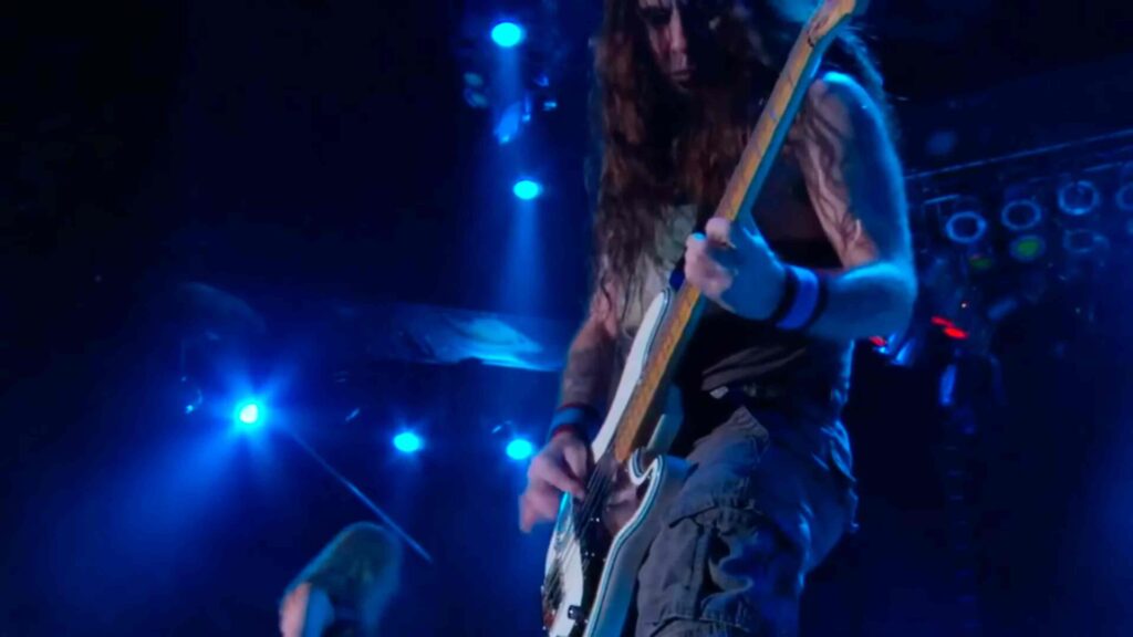 10 Rock and Metal Bands Inspired by Fantasy Books Heavy metal guitarist playing live beneath blue concert lighting.