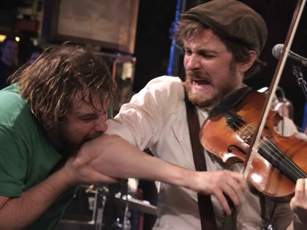 7 Crazy Behind-the-Scenes Moments That Happened During Live Concerts Concertgoer biting a viola player’s arm during a live performance at a crowded bar.
