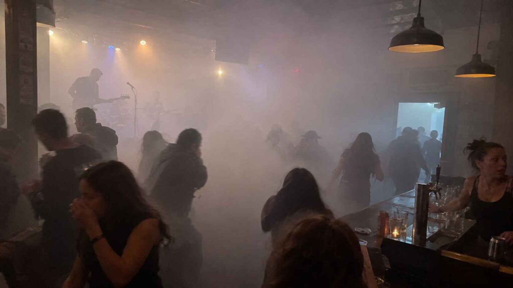 7 Crazy Behind-the-Scenes Moments That Happened During Live Concerts Thick fog fills a crowded bar during a live concert as people head toward the exit.