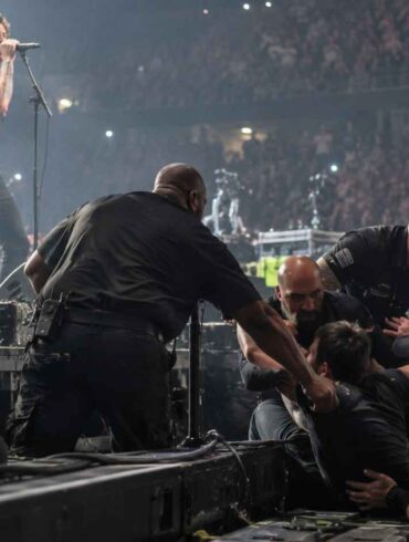 Behind-the-Scenes -Security guards removing an intruder from the stage during a crowded rock concert.