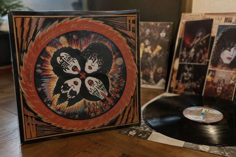 KISS Rock And Roll Over 50th Anniversary Box Set, Release Date and What Is Included KISS vinyl record and memorabilia displayed on a wooden table.