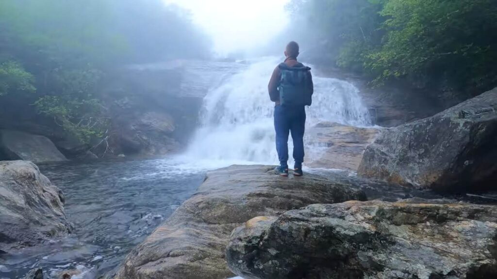 Why So Many Americans Are Moving to North Carolina Right Now? Hiker standing on rocks overlooking a waterfall in North Carolina's Blue Ridge Mountains.