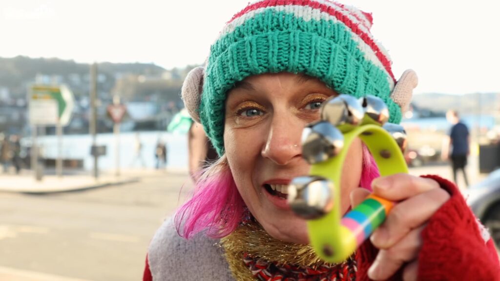 Woman wearing a colourful Christmas elf hat and holding festive bells during celebrations in Oban, Scotland.