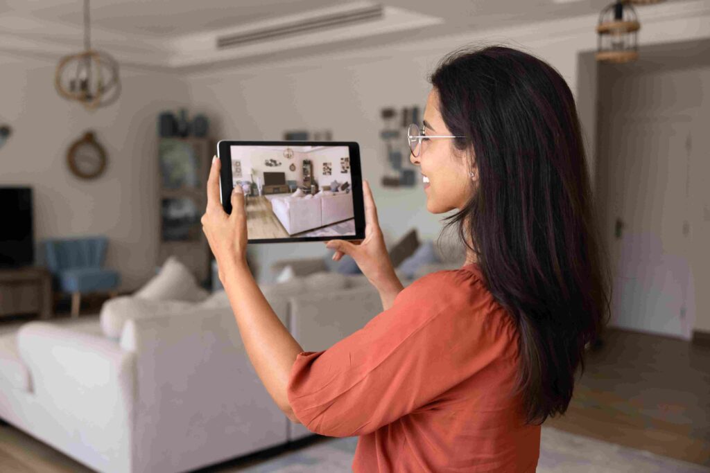 Seattle Housing Market 2026, Is Now a Better Time to Buy a House? Woman using a tablet to photograph a bright, furnished living room for a real estate listing.