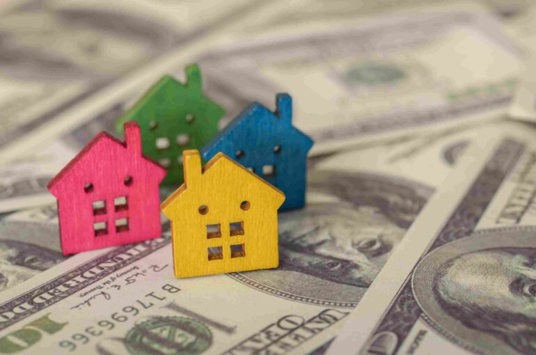 Colorful miniature houses arranged on US dollar bills.