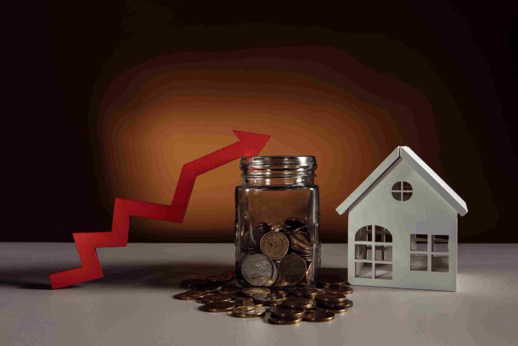 Seattle Housing Market 2026, Is Now a Better Time to Buy a House? Model house beside a coin-filled jar and an upward red arrow representing rising housing costs.